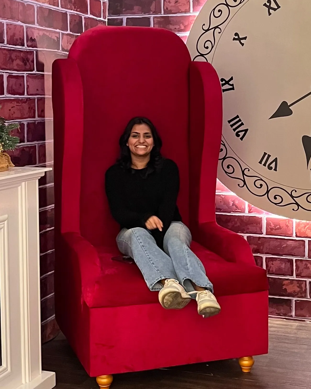 Keren smiling, sitting in an oversized red velvet armchair.