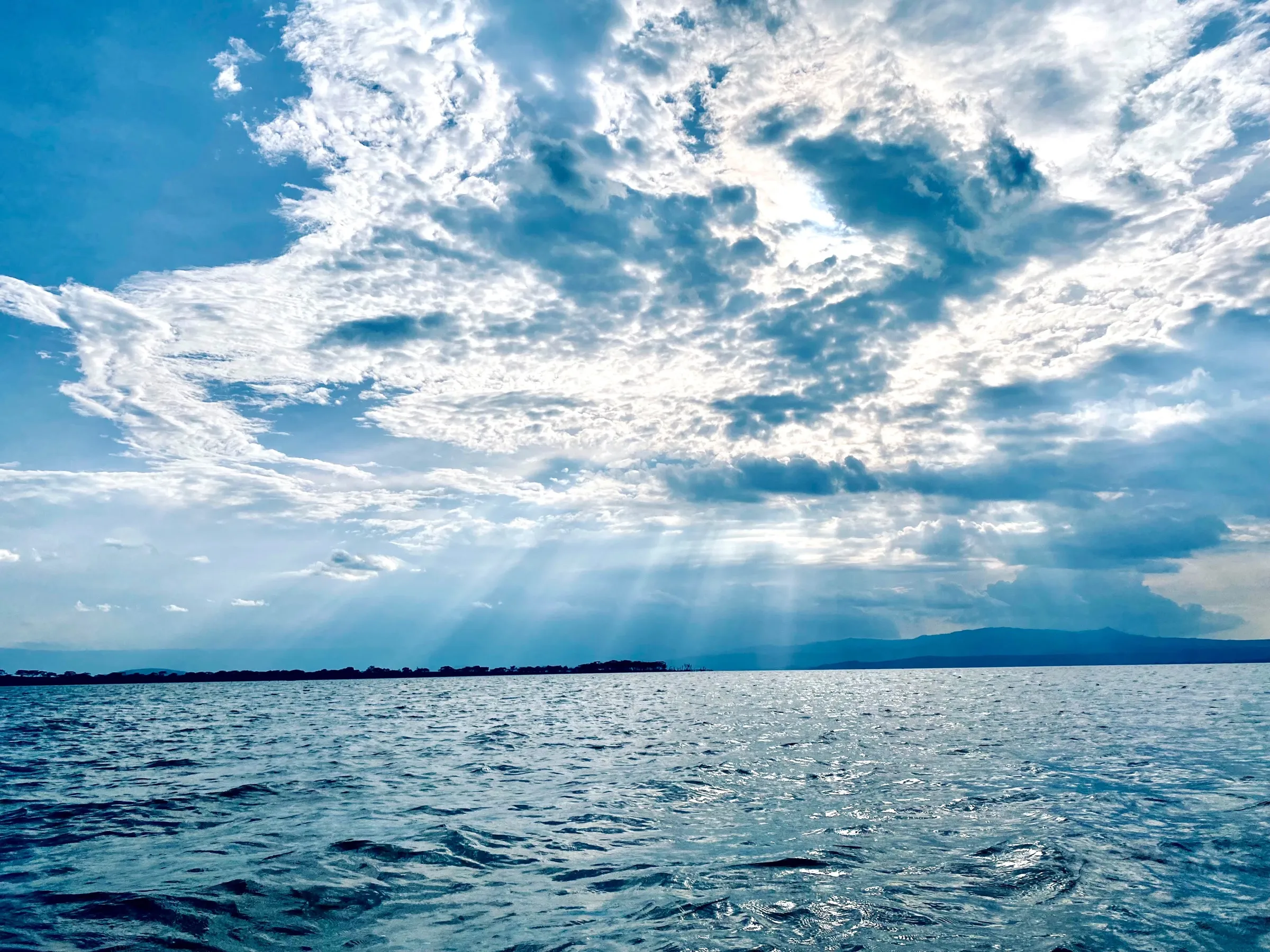 Sunbeams breaking through heavy clouds over a wide stretch of rippled water.