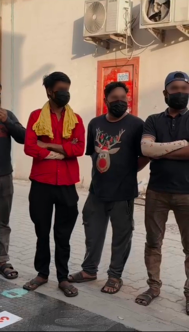Three welders stand in a row outside, arms crossed, wearing black face masks as part of the prop set.