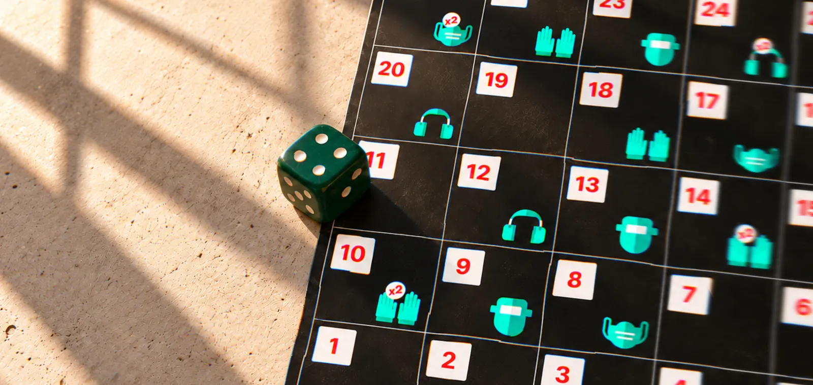 Sunlight and window shadows fall across the Weldo board and a dark green die: numbered squares from START at 1, with mint green PPE icons (welding helmets, headphones, gloves and masks) on some of them.
